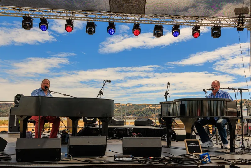 Two pianos on an outdoor festival stage under a blue sky