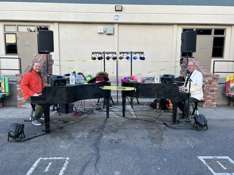 Daytime outdoor setup with two piano shells, PA speakers and a lighting tree