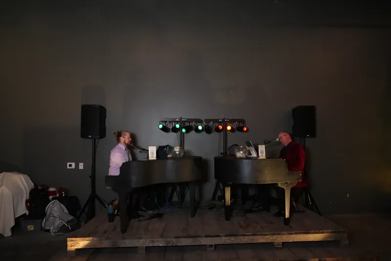 Two black grand piano shells facing each other on a stage with lights and speakers