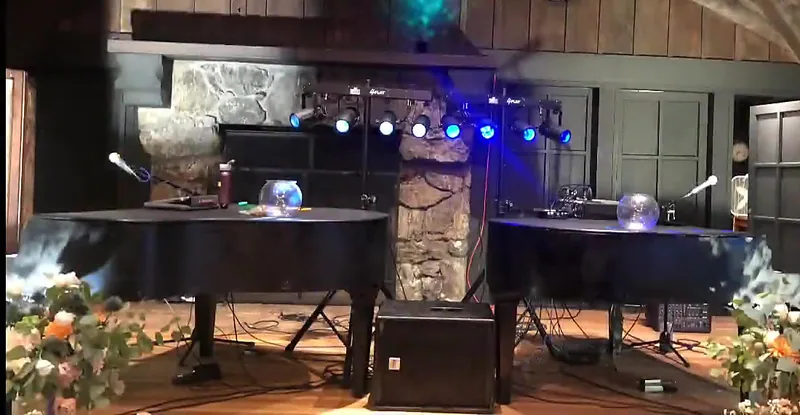 Two grand piano shells with stage lights and wedding flowers in a timber-beamed event hall